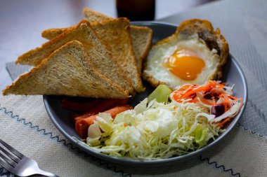 Kahvaltı, sahanda yumurta, kızarmış sosis, sebze salatası ve kahverengi ahşap bir masada tost ve Tayland kahvesi..