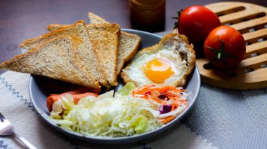 Kahvaltı, sahanda yumurta, kızarmış sosis, sebze salatası ve kahverengi ahşap bir masada tost ve Tayland kahvesi..