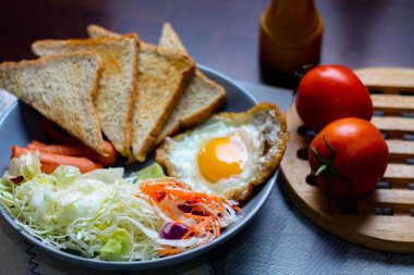 Kahvaltı, sahanda yumurta, kızarmış sosis, sebze salatası ve kahverengi ahşap bir masada tost ve Tayland kahvesi..