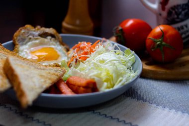 Kahvaltı, sahanda yumurta, kızarmış sosis, sebze salatası ve kahverengi ahşap bir masada tost ve Tayland kahvesi..