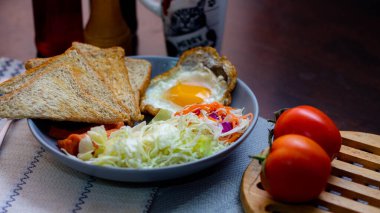 Kahvaltı, sahanda yumurta, kızarmış sosis, sebze salatası ve kahverengi ahşap bir masada tost ve Tayland kahvesi..