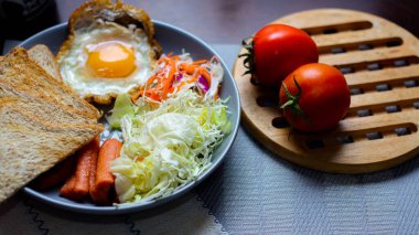 Kahvaltı, sahanda yumurta, kızarmış sosis, sebze salatası ve kahverengi ahşap bir masada tost ve Tayland kahvesi..