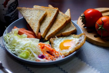 Kahvaltı, sahanda yumurta, kızarmış sosis, sebze salatası ve kahverengi ahşap bir masada tost ve Tayland kahvesi..