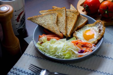 Kahvaltı, sahanda yumurta, kızarmış sosis, sebze salatası ve kahverengi ahşap bir masada tost ve Tayland kahvesi..