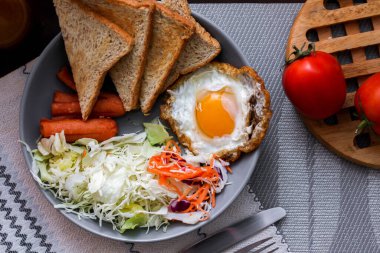 Kahvaltı, sahanda yumurta, kızarmış sosis, sebze salatası ve kahverengi ahşap bir masada tost ve Tayland kahvesi..
