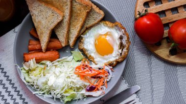 Kahvaltı, sahanda yumurta, kızarmış sosis, sebze salatası ve kahverengi ahşap bir masada tost ve Tayland kahvesi..