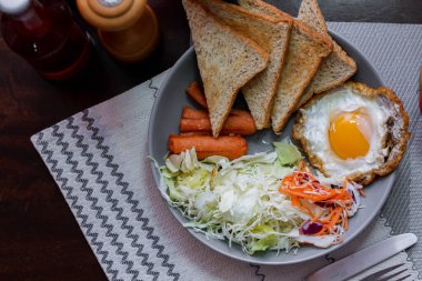 Kahvaltı, sahanda yumurta, kızarmış sosis, sebze salatası ve kahverengi ahşap bir masada tost ve Tayland kahvesi..