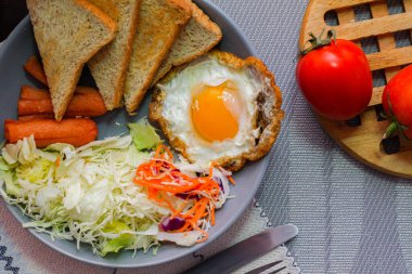 Kahvaltı, sahanda yumurta, kızarmış sosis, sebze salatası ve kahverengi ahşap bir masada tost ve Tayland kahvesi..