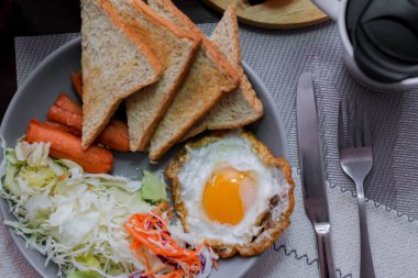 Kahvaltı, sahanda yumurta, kızarmış sosis, sebze salatası ve kahverengi ahşap bir masada tost ve Tayland kahvesi..