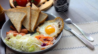 Kahvaltı, sahanda yumurta, kızarmış sosis, sebze salatası ve kahverengi ahşap bir masada tost ve Tayland kahvesi..