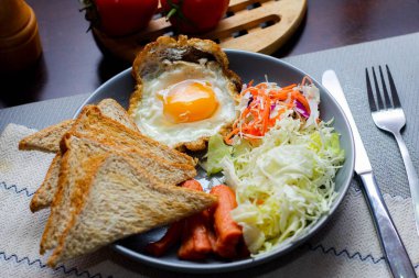 Kahvaltı, sahanda yumurta, kızarmış sosis, sebze salatası ve kahverengi ahşap bir masada tost ve Tayland kahvesi..