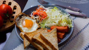 Kahvaltı, sahanda yumurta, kızarmış sosis, sebze salatası ve kahverengi ahşap bir masada tost ve Tayland kahvesi..