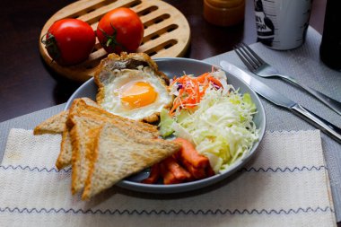 Kahvaltı, sahanda yumurta, kızarmış sosis, sebze salatası ve kahverengi ahşap bir masada tost ve Tayland kahvesi..