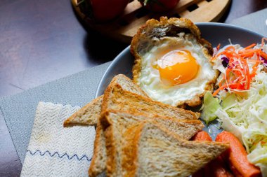 Kahvaltı, sahanda yumurta, kızarmış sosis, sebze salatası ve kahverengi ahşap bir masada tost ve Tayland kahvesi..