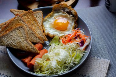 Kahvaltı, sahanda yumurta, kızarmış sosis, sebze salatası ve kahverengi ahşap bir masada tost ve Tayland kahvesi..