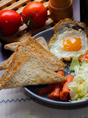 Kahvaltı, sahanda yumurta, kızarmış sosis, sebze salatası ve kahverengi ahşap bir masada tost ve Tayland kahvesi..