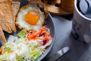 Kahvaltı, sahanda yumurta, kızarmış sosis, sebze salatası ve kahverengi ahşap bir masada tost ve Tayland kahvesi..