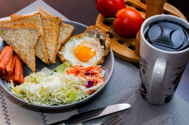 Kahvaltı, sahanda yumurta, kızarmış sosis, sebze salatası ve kahverengi ahşap bir masada tost ve Tayland kahvesi..
