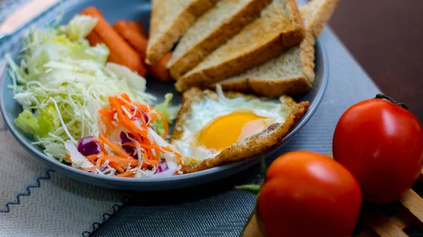 Kahvaltı, sahanda yumurta, kızarmış sosis, sebze salatası ve kahverengi ahşap bir masada tost ve Tayland kahvesi..