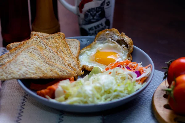 Kahvaltı, sahanda yumurta, kızarmış sosis, sebze salatası ve kahverengi ahşap bir masada tost ve Tayland kahvesi..