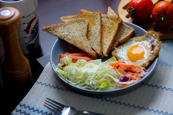 Kahvaltı, sahanda yumurta, kızarmış sosis, sebze salatası ve kahverengi ahşap bir masada tost ve Tayland kahvesi..