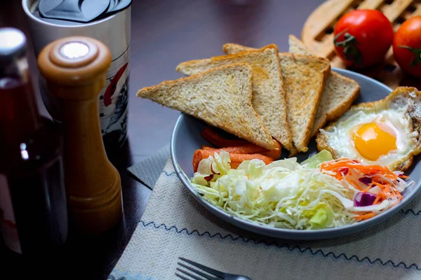 Kahvaltı, sahanda yumurta, kızarmış sosis, sebze salatası ve kahverengi ahşap bir masada tost ve Tayland kahvesi..