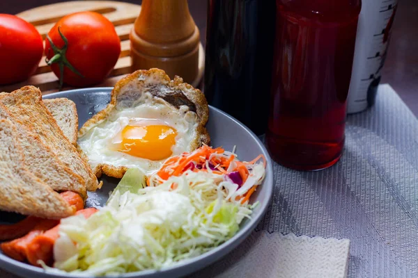 Kahvaltı, sahanda yumurta, kızarmış sosis, sebze salatası ve kahverengi ahşap bir masada tost ve Tayland kahvesi..