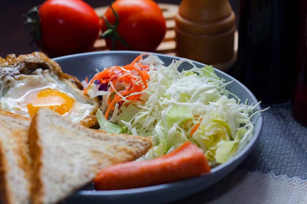 Kahvaltı, sahanda yumurta, kızarmış sosis, sebze salatası ve kahverengi ahşap bir masada tost ve Tayland kahvesi..