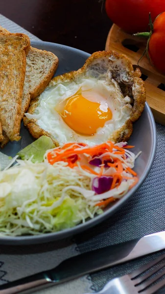 Kahvaltı, sahanda yumurta, kızarmış sosis, sebze salatası ve kahverengi ahşap bir masada tost ve Tayland kahvesi..