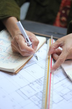 Asyalı kadın mühendislerin elleri inşaat alanındaki çizimler üzerinde çalışıyor..