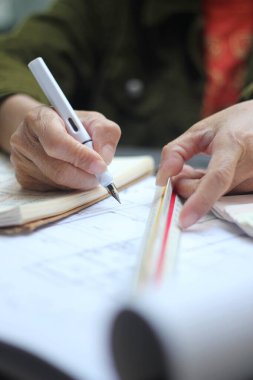 Asyalı kadın mühendislerin elleri inşaat alanındaki çizimler üzerinde çalışıyor..