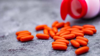 Turuncu kapsül ve ilaç şişeleri gri masaya yerleştirildi. Arkasından ışık geliyordu.