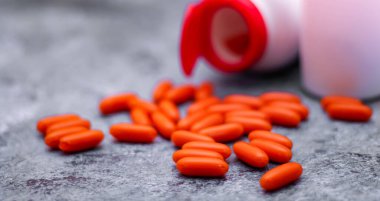 Turuncu kapsül ve ilaç şişeleri gri masaya yerleştirildi. Arkasından ışık geliyordu.