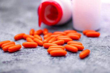 Turuncu kapsül ve ilaç şişeleri gri masaya yerleştirildi. Arkasından ışık geliyordu.