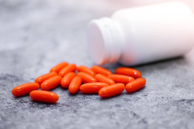 Turuncu kapsül ve ilaç şişeleri gri masaya yerleştirildi. Arkasından ışık geliyordu.