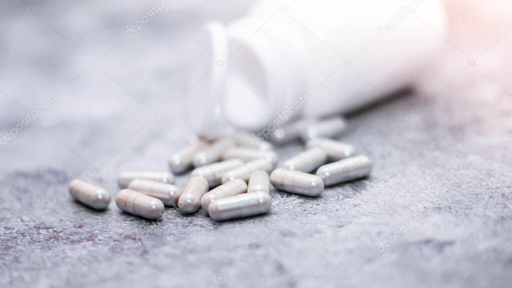 The gray capsule and pill bottles were placed on the gray table with light coming from behind.