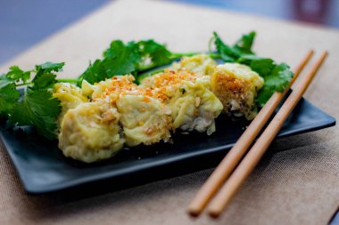 Çin Buharlı Hamur köftesi, ahşap bir masada siyah bir tabakta servis edilir. Kişniş ile birlikte.