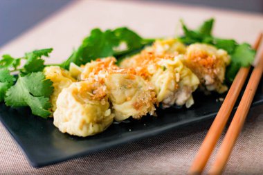 Çin Buharlı Hamur köftesi, ahşap bir masada siyah bir tabakta servis edilir. Kişniş ile birlikte.