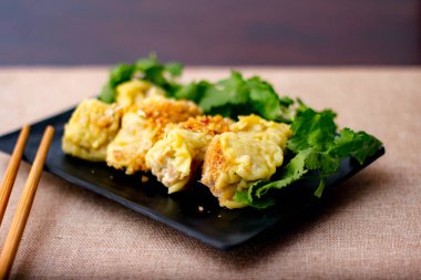 Çin Buharlı Hamur köftesi, ahşap bir masada siyah bir tabakta servis edilir. Kişniş ile birlikte.