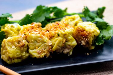 Çin Buharlı Hamur köftesi, ahşap bir masada siyah bir tabakta servis edilir. Kişniş ile birlikte.