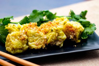 Çin Buharlı Hamur köftesi, ahşap bir masada siyah bir tabakta servis edilir. Kişniş ile birlikte.