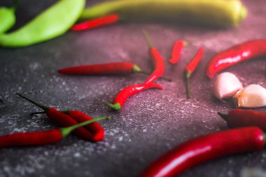 Kırmızı biber ve yeşil biber, gri masaya yayılmış sarımsak mutfakta pişirmeye hazır..