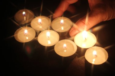 Bir adamın eli ahşap bir masada birkaç mum yakıyor.