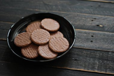 Çikolata aromalı kurabiyeler, ahşap bir masada siyah bir tabakta servis edilir..
