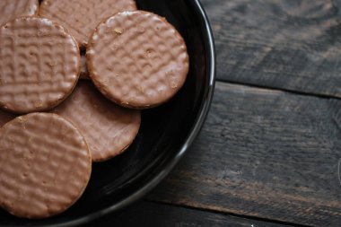 Çikolata aromalı kurabiyeler, ahşap bir masada siyah bir tabakta servis edilir..