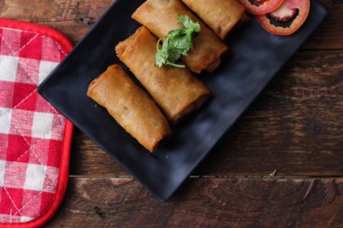 Tayland 'da kahverengi ahşap bir masada doğranmış domatesli siyah kare bir tabakta kızarmış börek servis ediliyor..