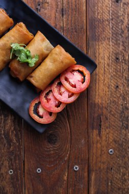 Tayland 'da kahverengi ahşap bir masada doğranmış domatesli siyah kare bir tabakta kızarmış börek servis ediliyor..