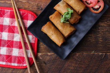 Tayland 'da kahverengi ahşap bir masada doğranmış domatesli siyah kare bir tabakta kızarmış börek servis ediliyor..
