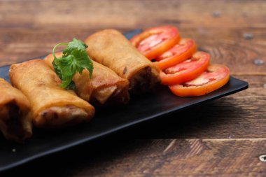 Tayland 'da kahverengi ahşap bir masada doğranmış domatesli siyah kare bir tabakta kızarmış börek servis ediliyor..