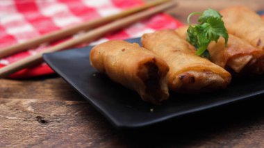 Tayland 'da kahverengi ahşap bir masada doğranmış domatesli siyah kare bir tabakta kızarmış börek servis ediliyor..